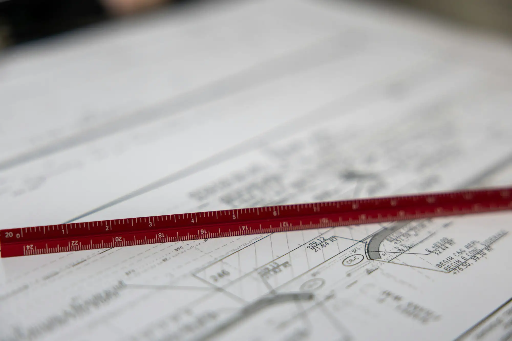 Red scale ruler resting on printed building plans, the stage where a builder prices the job and sets the deposit