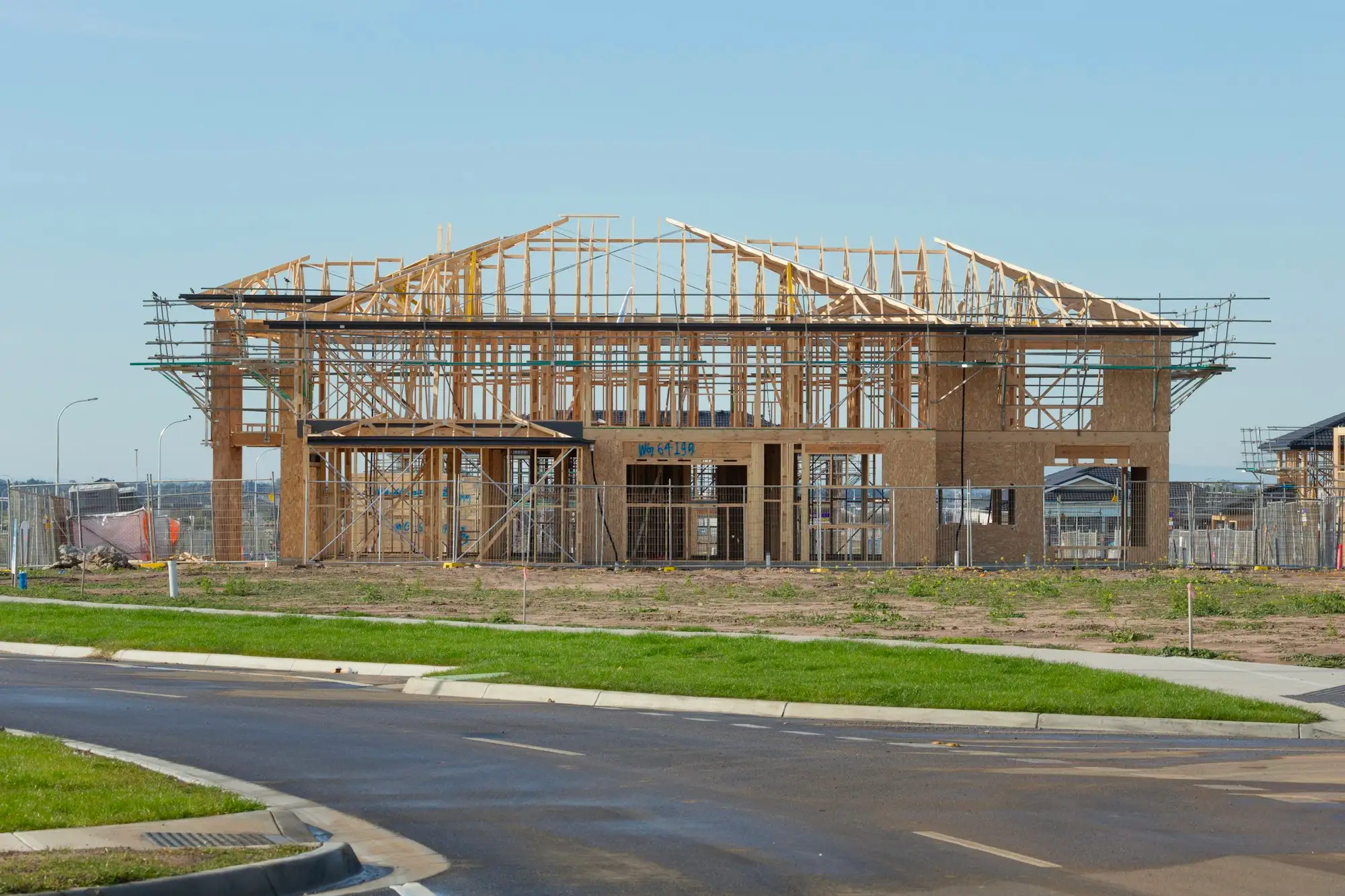 Two storey timber house frame with scaffolding and temporary fencing on a new Australian housing estate, the stage where variations often come up