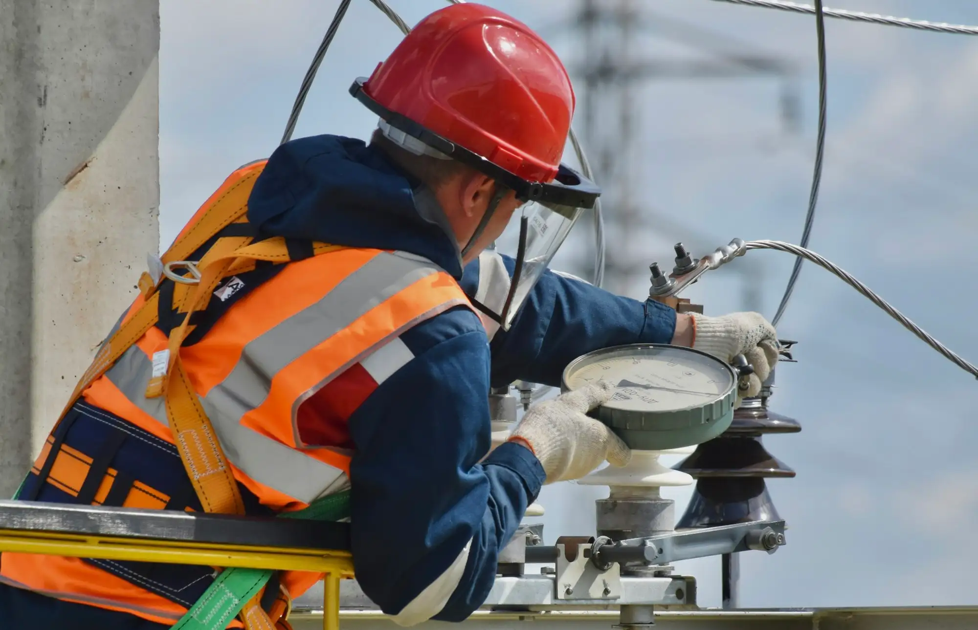 Worker in a red hard hat, hi-vis vest and fall arrest harness working at height from a platform rail